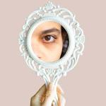 Women looking into mirror to observe under-eye dark circles.